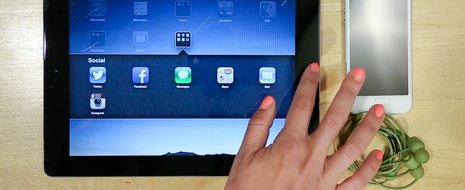 A tablet with a hand hovering over the home button has an array of icons displayed on the screen